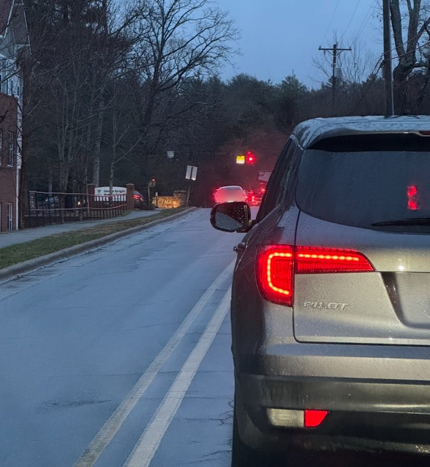 At dawn, a vehicle crosses the double yellow line on Overlook Road toward a red signal while an SUV waits in the queue