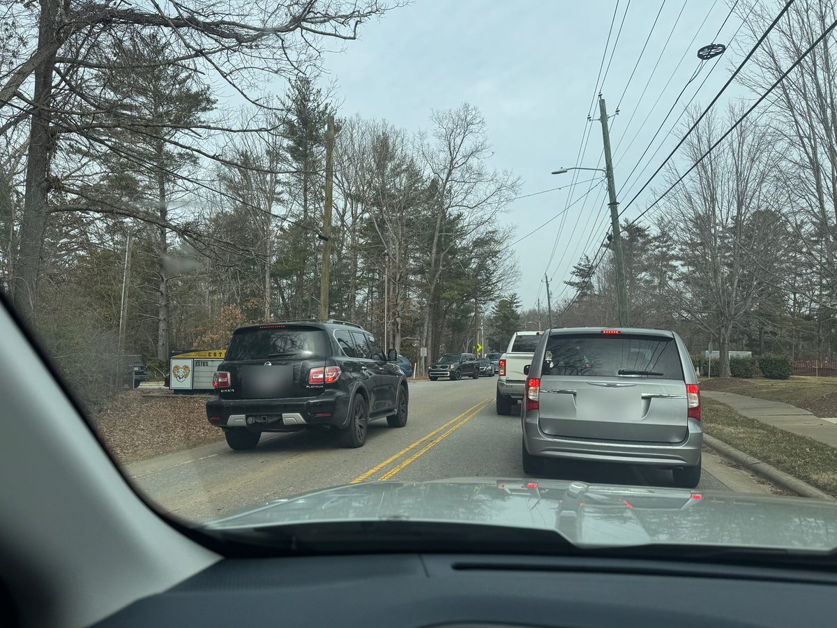 An SUV crosses the double yellow line on Overlook Road to pass a minivan stopped to turn left into Estes Elementary; the school sign is visible on the left